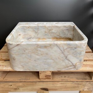 May include: Rectangular marble sink with rounded edges. The sink has a cream and tan colour palette with veining throughout. The sink has three pre-drilled tap holes and is set on a wooden pallet.
