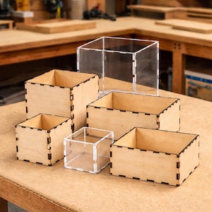 May include: A collection of wooden and clear acrylic boxes of varying sizes. The wooden boxes are light brown with dark brown joints. The clear acrylic boxes are transparent. The boxes are arranged on a light brown surface.