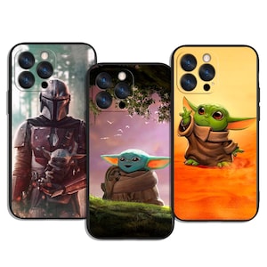 Op de afbeelding: Drie telefoonhoesjes met Star Wars-personages. Eén hoesje toont The Mandalorian en Grogu, een ander Grogu op een grasheuvel en de derde Grogu tegen een oranje achtergrond. De hoesjes hebben zwarte randen en camera-uitsparingen.