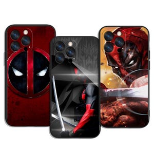 Op de afbeelding: Drie zwarte telefoonhoesjes met Deadpool-ontwerpen. De hoesjes tonen Deadpool's masker, een volledige lichaamsillustratie met zwaarden en een close-up van zijn gezicht. De hoesjes hebben een zwarte rand en zijn ontworpen voor een telefoon met meerdere cameralenzen.