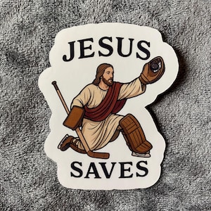 Op de afbeelding: Een sticker met een illustratie van Jezus als hockeydoelman. Hij draagt een wit gewaad, bruine pads en een handschoen, met een hockeystick. De tekst "JESUS SAVES" staat boven en onder de afbeelding.