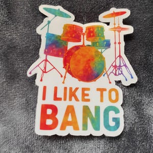 May include: A sticker depicting a drum kit with a vibrant tie-dye design. The phrase "I LIKE TO BANG" is written beneath the drums in a rainbow gradient. The sticker has a white border.