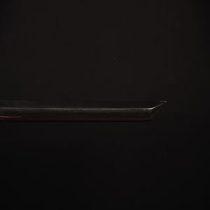 Pu&ograve; includere: Primo piano di un oggetto metallico scuro con un bordo affilato e angolato. L'oggetto sembra essere una lama o uno strumento simile, forse parte di un elemento pi&ugrave; grande. La superficie riflette la luce, creando riflessi sullo sfondo scuro.