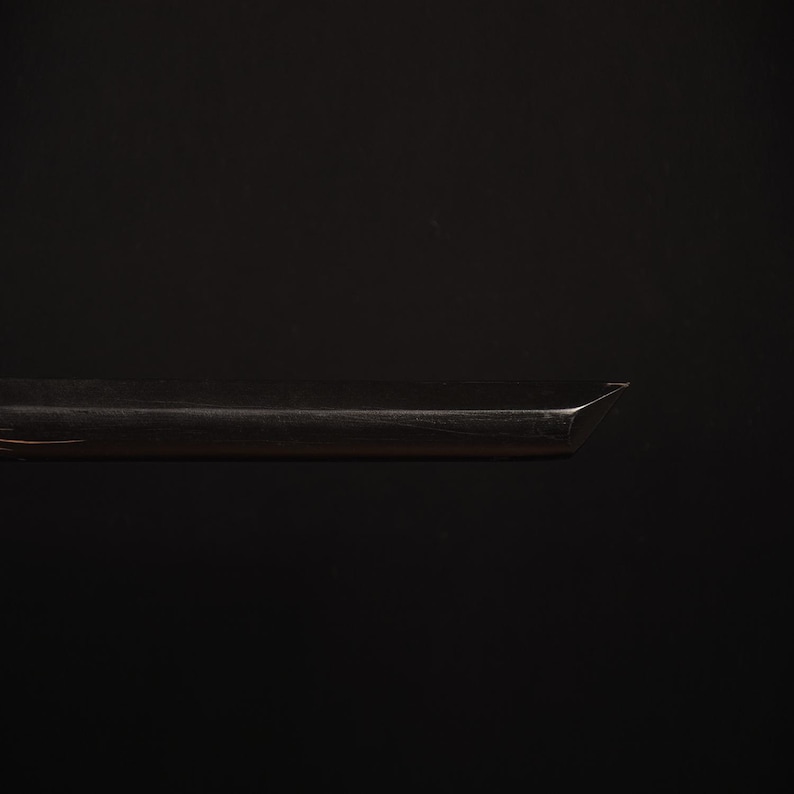 Pu&ograve; includere: Primo piano di un oggetto metallico scuro con un bordo affilato e angolato. L'oggetto sembra essere una lama o uno strumento simile, forse parte di un elemento pi&ugrave; grande. La superficie riflette la luce, creando riflessi sullo sfondo scuro.
