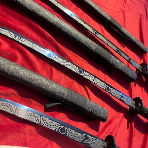 May include: Several black swords with ornate silver designs on the blades and handles are displayed against a red background. The blades have a blue hue. The handles are wrapped in a textured pattern.