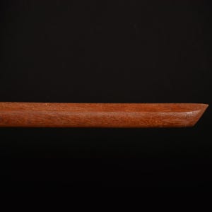 Pu&ograve; includere: Primo piano di un vassoio di legno con finitura marrone rossiccio scuro. Il vassoio ha una forma rettangolare con un bordo smussato su un'estremit&agrave;. La venatura del legno &egrave; visibile e il vassoio sembra fatto a mano.
