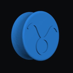 May include: A blue, circular Taurus zodiac symbol with a bull's head design. The symbol is carved into the surface of the disc. The background is black.