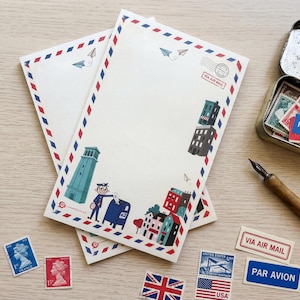 Peut inclure: Deux feuilles de papier à lettres avec une bordure rouge, blanche et bleue et des illustrations de bâtiments, d'une tour et d'un facteur. Des timbres, une boîte en métal et un stylo sont également visibles. Le papier à lettres porte les mots "VIA AIR MAIL".