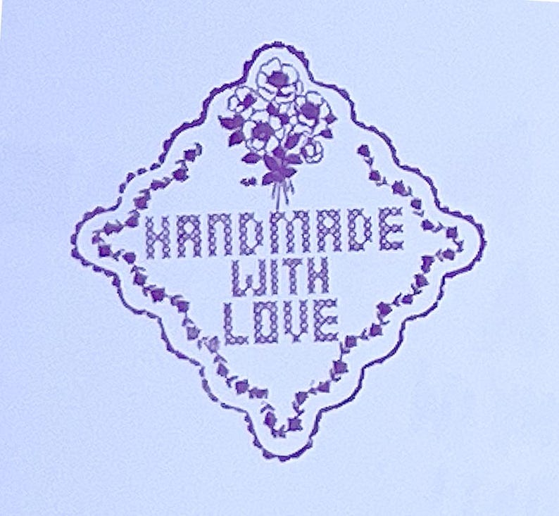 Puede incluir: Un dise&ntilde;o floral morado y blanco con las palabras "HANDMADE WITH LOVE" en un marco en forma de diamante. El texto est&aacute; en estilo de punto de cruz, con un ramo de flores en la parte superior.