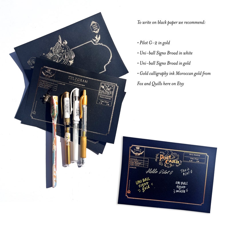 May include: A collection of black stationery items with gold accents, including postcards and telegrams. Several pens are arranged next to the stationery. The text on the postcard reads "Hello Pilot G" and "Uni-ball Signo - gold".