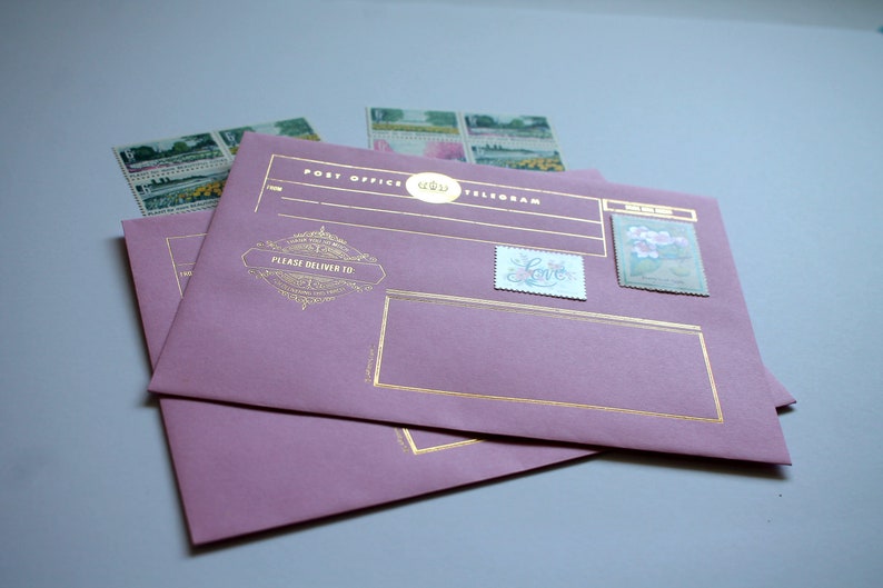 Może przedstawiać: Dwie mauve koperty telegram&oacute;w ze złotymi akcentami i ozdobnymi znaczkami pocztowymi. Na kopertach widnieją napisy "Post Office Telegram" i "Please Deliver To". Widocznych jest kilka znaczk&oacute;w.