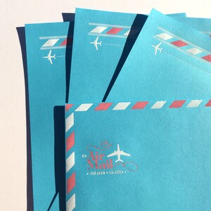 May include: Blue paper stationery with a red and white striped border and a white airplane graphic. The paper has the text "Via Air Mail" with a small airplane graphic and the text "Par Avion - Via Aerea".