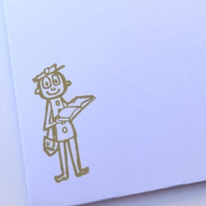 Puede incluir: Ilustración en tinta dorada de una persona sosteniendo un libro sobre un fondo blanco. La figura está dibujada con líneas simples y una expresión amigable, llevando una bandolera. La imagen está sobre papel blanco.