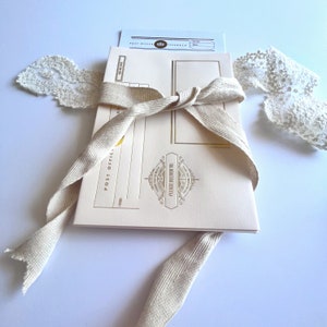 May include: A cream-colored envelope with a gold ribbon tied around it. The envelope has a gold design with the text "Post Office" and "Please Deliver To" on the front.