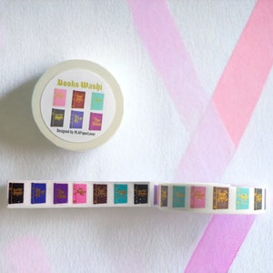 K&ouml;nnte beinhalten: Eine Rolle wei&szlig;es Washi-Klebeband mit einem goldenen Design von Buchumschl&auml;gen. Das Band ist abgewickelt und zeigt das Design der Buchumschl&auml;ge. Die Rolle des Bandes ist mit "Books Washi" und "Designed by PLA Paper Lover" beschriftet.