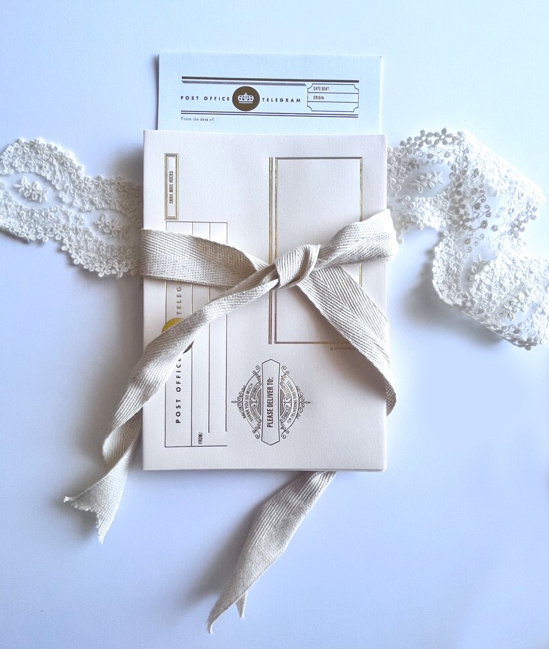 May include: A cream-colored postcard with gold accents and a brown ribbon tied around it. The postcard has the words "Post Office Telegram" printed on it. The postcard is on a white background.