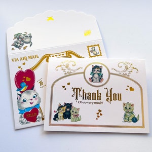 Puede incluir: Un juego de tarjetas de felicitaci&oacute;n y un sobre de estilo vintage con adorables ilustraciones de gatitos. El sobre dice "VIA AIR MAIL" y la tarjeta dice "Thank You" en elegantes letras doradas. El dise&ntilde;o incluye corazones y un sello.