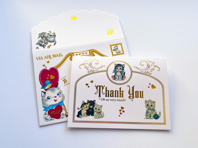 Puede incluir: Un juego de tarjetas de felicitaci&oacute;n y un sobre de estilo vintage con adorables ilustraciones de gatitos. El sobre dice "VIA AIR MAIL" y la tarjeta dice "Thank You" en elegantes letras doradas. El dise&ntilde;o incluye corazones y un sello.