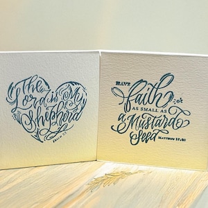 May include: Two square cards with inspirational quotes. One card features a heart-shaped design with the text "The Lord is My Shepherd." The other card has the phrase "Have faith as small as a mustard seed."