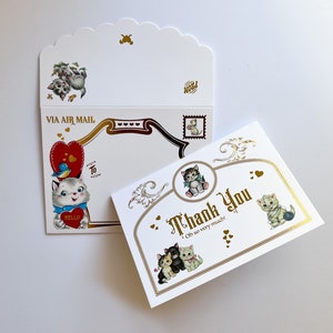 Puede incluir: Un juego de papeler&iacute;a de estilo vintage con ilustraciones de gatitos. El juego incluye un sobre con borde festoneado con el texto "Via Air Mail" y una tarjeta de "Thank You" con detalles dorados y la frase "Oh so very much!"