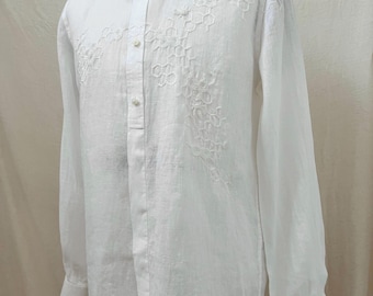 May include: A white long-sleeve shirt with intricate embroidered floral patterns on the front. The shirt features a classic collar, button-down closure, and buttoned cuffs. The fabric appears to be lightweight, possibly linen or a similar material.