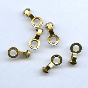 May include: Five gold-toned metal eyelet caps with a round hole and a small ball on one end. The eyelet caps are designed for use with fabric or leather.