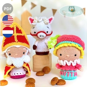 Op de afbeelding: Een verzameling van drie gehaakte poppen. Eén pop is gekleed als Sinterklaas in een rood en goudkleurig kostuum, een witbebaarde pop met een rode hoed. Een andere is een wit schaap met een rode bril. De derde pop heeft een roze hoed en een kleurrijke outfit.