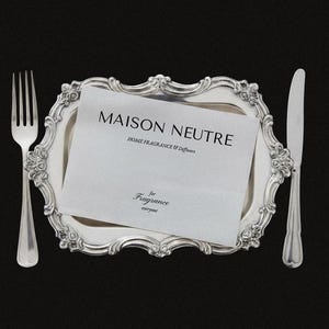 May include: A silver fork and knife flank a decorative silver tray holding a white card with the text "MAISON NEUTRE HOME FRAGRANCE & Diffusers" and "for Fragrance everyone" on a black background.