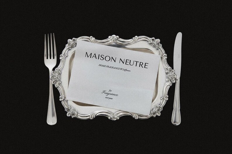 May include: A silver fork and knife flank a decorative silver tray holding a white card with the text "MAISON NEUTRE HOME FRAGRANCE & Diffusers" and "for Fragrance everyone" on a black background.