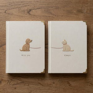 May include: Two off-white hardcover books with gold-tone metal corner protectors. The left book features an embroidered tan dog with a red leash and the text "With you". The right book features an embroidered tan cat with a red leash and the text "Always".