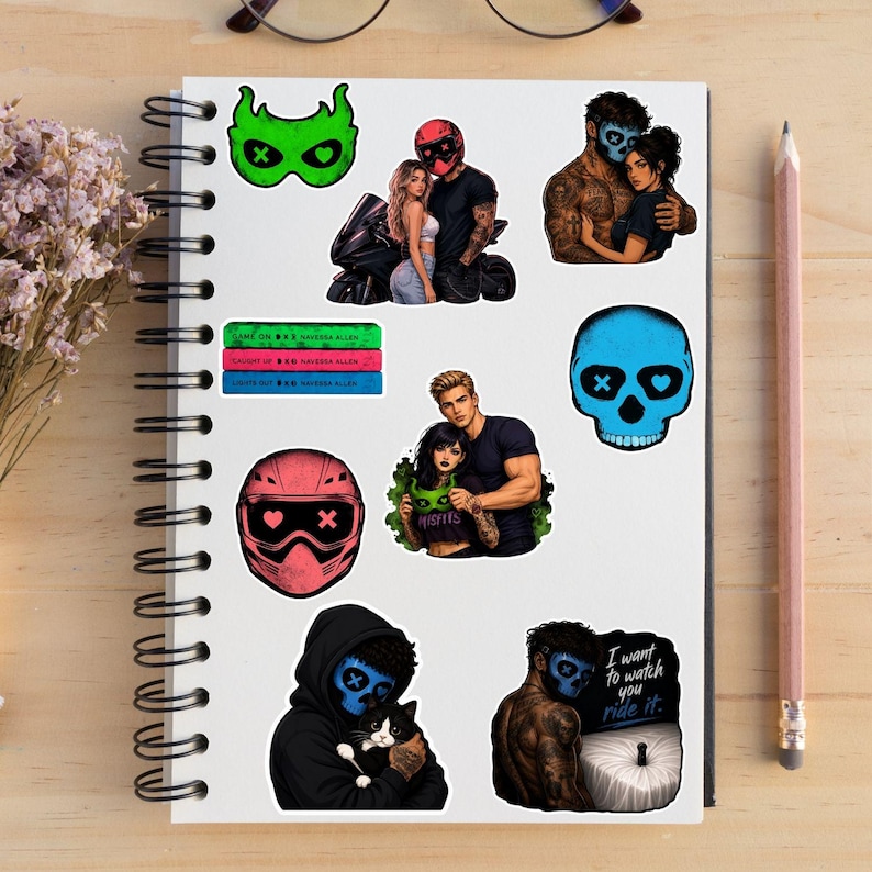 May include: A collection of stickers on a spiral notebook. The stickers feature illustrations of couples, skulls, and motorcycle helmets. Some stickers have the text "Misfits" and "I want to watch you ride it."