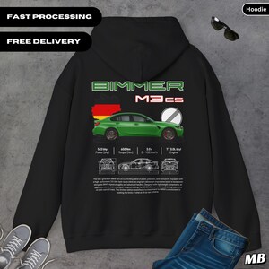 Puede incluir: Sudadera con capucha negra con un gráfico de coche verde y el texto "BIMMER M3CS". El diseño incluye especificaciones técnicas y un contorno de la bandera alemana. La sudadera también tiene el texto "FAST PROCESSING" y "FREE DELIVERY".