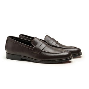 May include: A pair of dark brown leather penny loafers. The shoes have a classic design with a rounded toe, a strap across the vamp, and a low heel. White stitching accents the sole.
