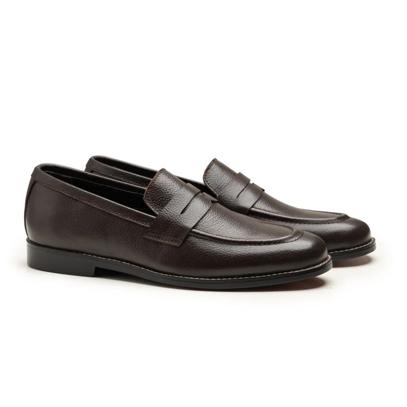 May include: A pair of dark brown leather penny loafers. The shoes have a classic design with a rounded toe, a strap across the vamp, and a low heel. White stitching accents the sole.