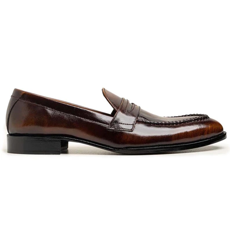 May include: A brown leather loafer with a glossy finish. The shoe features a classic penny strap design and a black sole. The leather has a rich, polished appearance, and the shoe is designed for formal or business attire.