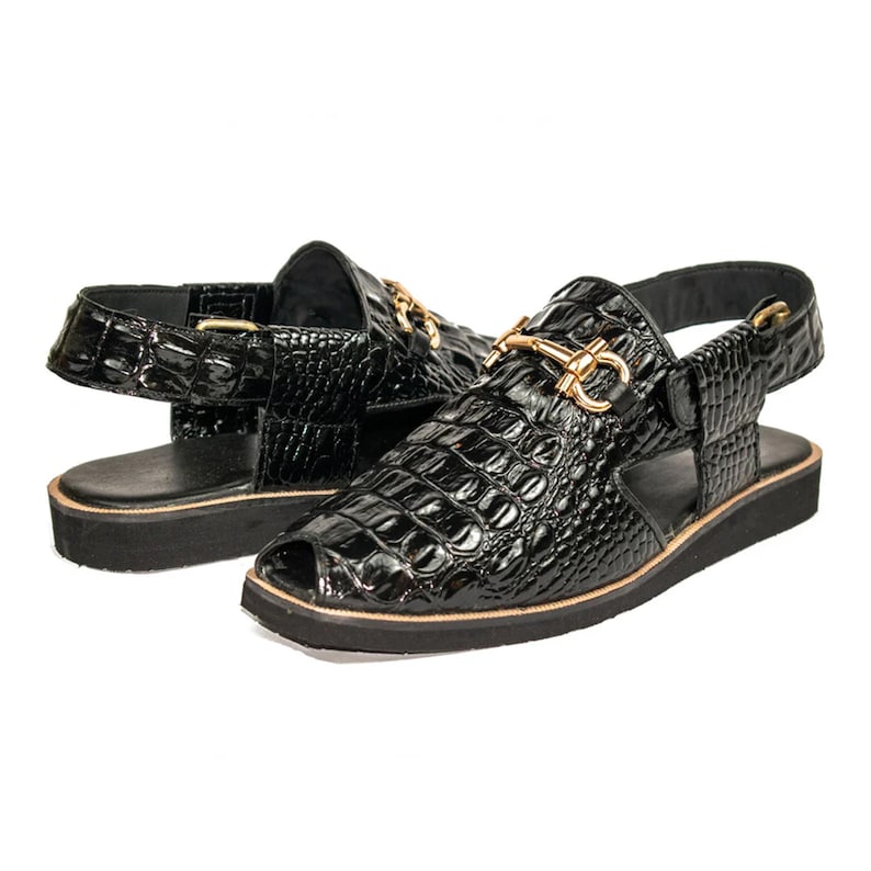 Op de afbeelding: Een paar zwarte sandalen met open teen en een glanzende krokodillenstructuur. De sandalen hebben goudkleurige details en een dikke, zwarte zool. Het ontwerp omvat een enkelbandje.