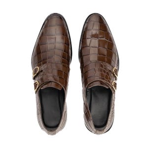 K&ouml;nnte beinhalten: Ein Paar braune Lederschuhe mit Krokodiltextur. Die Schuhe haben ein Design mit doppeltem Monk-Riemen und goldfarbenen Schnallen. Die Schuhe werden von oben betrachtet und zeigen ihr poliertes Aussehen.