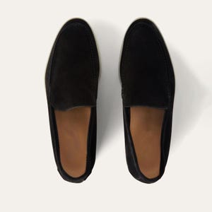 K&ouml;nnte beinhalten: Ein Paar schwarze Wildleder-Loafer mit runder Spitze und Slip-on-Design. Die Schuhe haben eine hellfarbene Sohle und ein braunes Innenfutter. Das Bild ist aus der Vogelperspektive aufgenommen und zeigt die Schuhe.