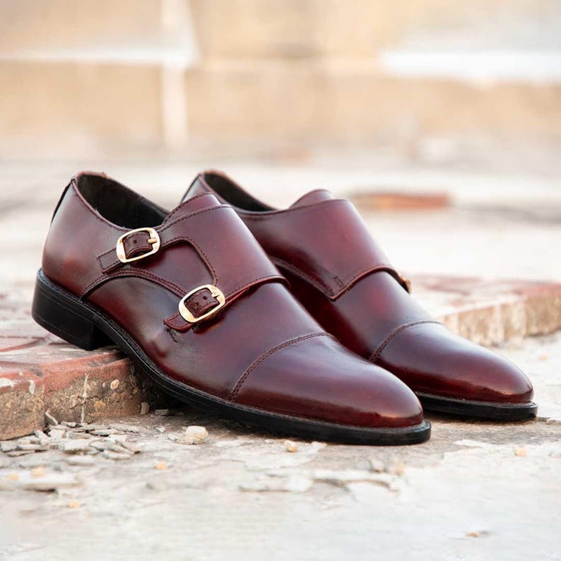 Peut inclure: Paire de chaussures &agrave; double boucle en cuir bordeaux avec boucles dor&eacute;es. Finition polie et design classique, adapt&eacute;es aux tenues formelles ou professionnelles. Longueur d'environ 30 cm.