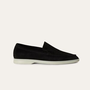 K&ouml;nnte beinhalten: Schwarzer Wildleder-Loafer mit wei&szlig;er Sohle. Der Schuh hat ein klassisches Slip-on-Design mit runder Spitze und niedrigem Absatz. Dieses Schuhwerk eignet sich f&uuml;r l&auml;ssige oder halbformelle Anl&auml;sse.