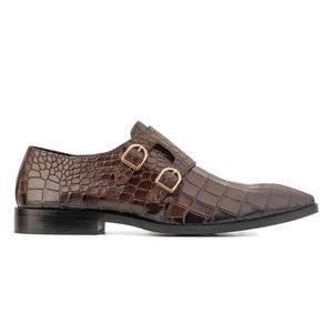K&ouml;nnte beinhalten: Brauner Lederschuh mit Krokodiltextur und spitzer Zehenpartie. Der Schuh hat zwei goldfarbene Schnallen und eine schwarze Sohle. Ein klassischer Stil f&uuml;r formelle Anl&auml;sse.