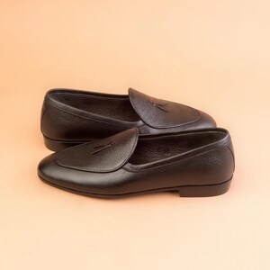 May include: A pair of black leather loafers with a textured finish. The shoes have a slip-on design with a rounded toe and a decorative tassel detail on the vamp. The loafers are set against a neutral background.