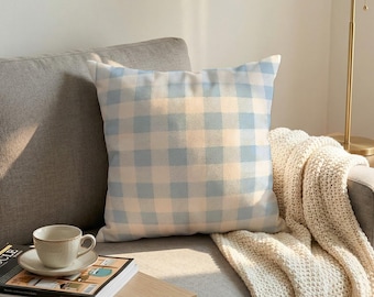 May include: A square throw cushion featuring a light blue and white gingham check pattern. The cushion has a soft, fabric texture and is displayed in a neutral setting, showcasing the repeating grid design across the entire front surface.