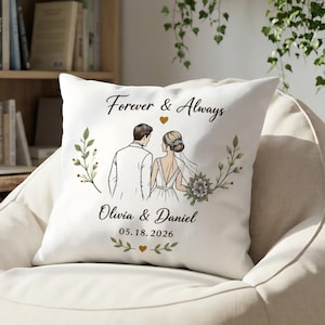 Könnte beinhalten: Ein weißes quadratisches Kissen mit einer gedruckten Illustration eines Paares in Hochzeitskleidung, dem Text Forever & Always, Olivia & Daniel und 05.18.2026, akzentuiert durch grüne botanische Zweige und kleine goldene Herzsymbole.