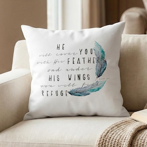 May include: A white square cushion featuring the text "HE will cover YOU with His FEATHERS and under HIS WINGS you will find REFUGE" in black script. Two teal watercolour feathers are on the right side.