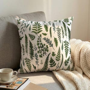 May include: A square throw cushion featuring a white background with a repeating pattern of various green fern leaves and botanical foliage in shades of dark forest green, sage, and olive, arranged in a dense, vertical, and scattered orientation.