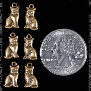 Puede incluir: Seis abalorios de gato de metal de color dorado antiguo, cada uno del tamaño de una moneda de 25 centavos de dólar estadounidense, con un bucle para colgar.