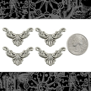 May include: Four silver-toned metal decorative embellishments in the shape of a stylized, ornate, curved arch. The embellishments are approximately the size of a US quarter.