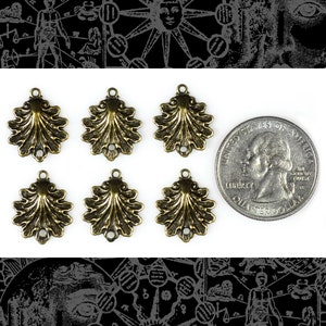 May include: Six antique brass-colored shell-shaped charms with a quarter for size comparison. Each charm has a loop at the top and two holes at the bottom. The charms are arranged on a white background.