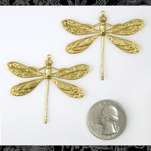 May include: Two gold-tone metal dragonfly charms with intricate details. The charms are approximately 2 inches long and have a loop at the top for attaching to jewelry or other crafts.